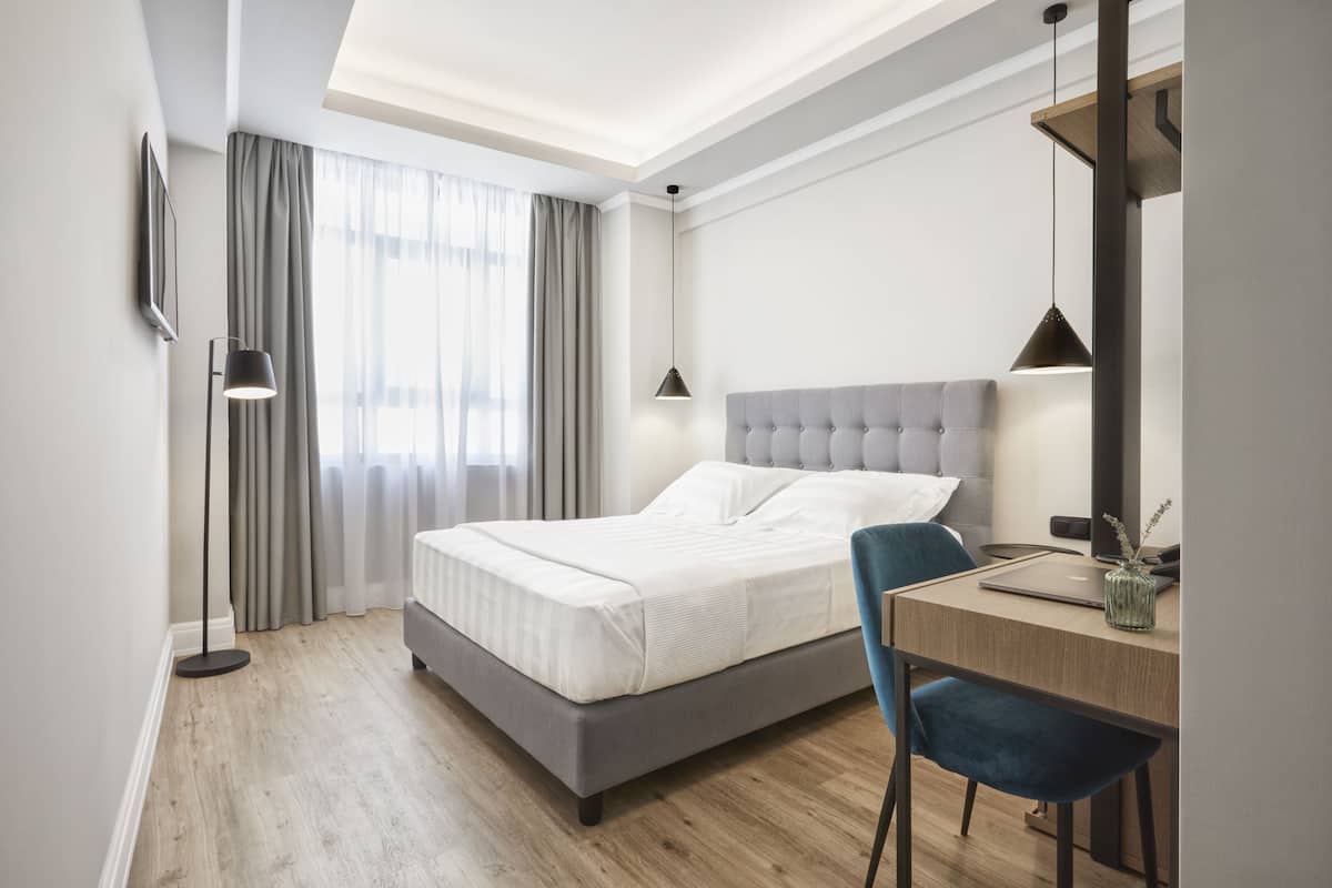 Une chambre d’hôtel moderne avec un grand lit, un bureau avec un ordinateur portable et une chaise.