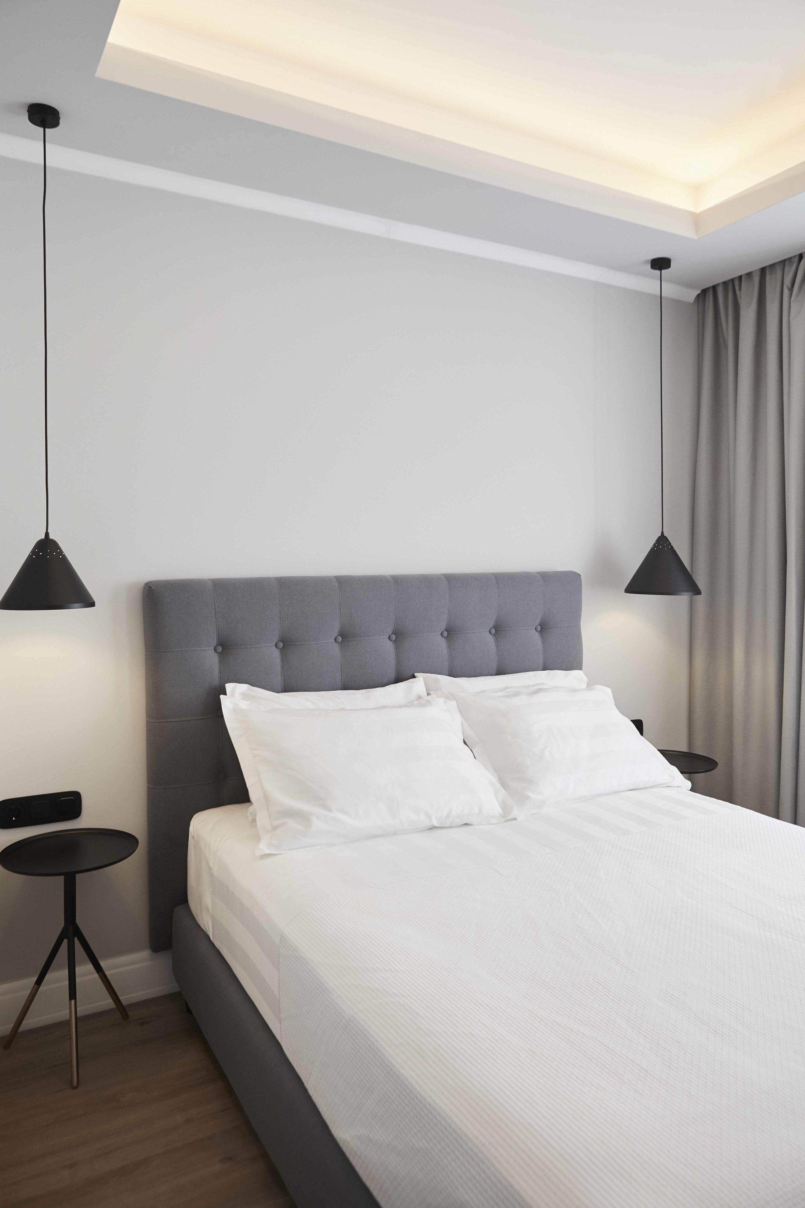Quarto de hotel moderno com uma cama grande, duas mesas de cabeceira e iluminação pendente.