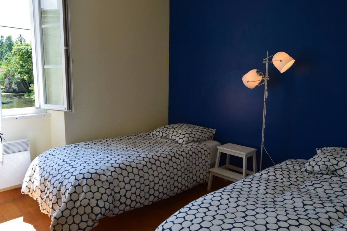 A bedroom with two beds, a window, and a floor lamp.