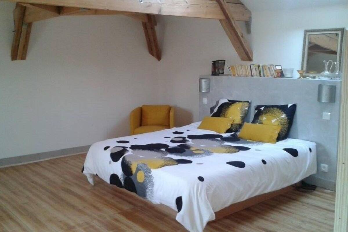A bedroom with a bed, a chair, wooden beams, a bookshelf, and a mirror.