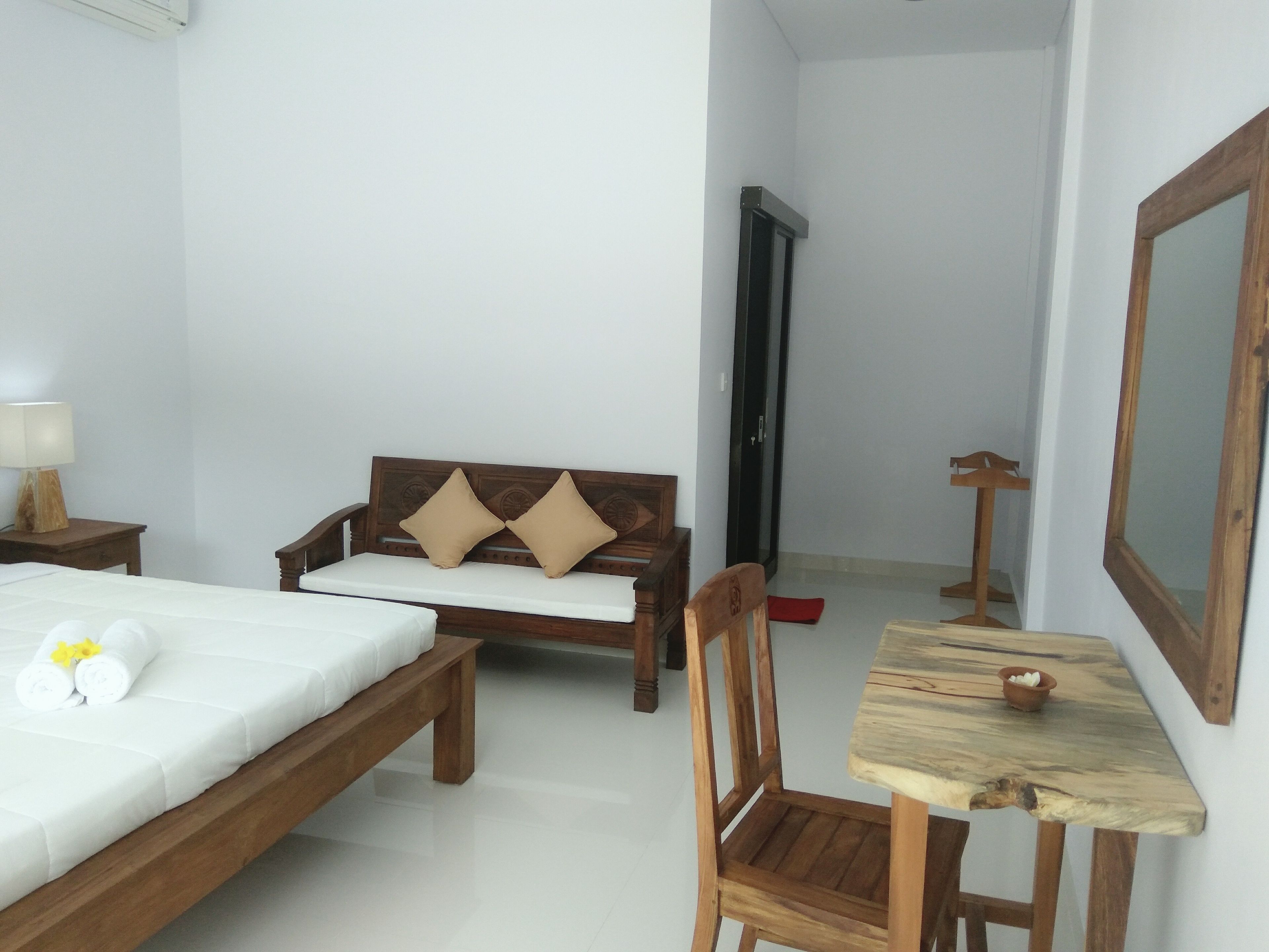 A hotel room with a bed, a wooden sofa with cushions, a wooden chair, a small table, and a mirror.