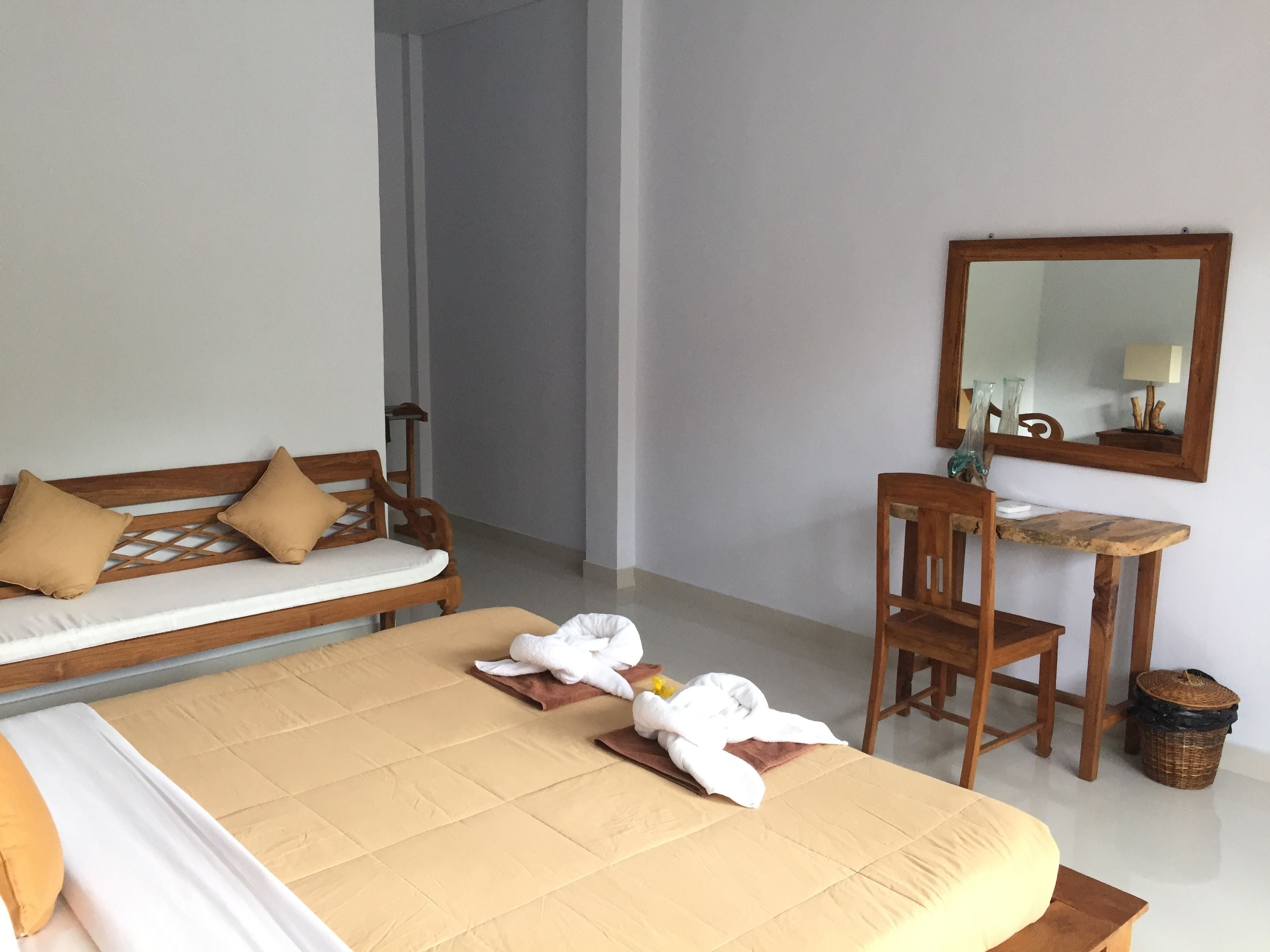 A hotel room with a bed, a wooden bench, a small table with a mirror, and a chair.