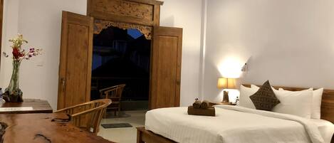 A bedroom with a wooden bed, a nightstand with a lamp, a wooden chair, and a rustic table.