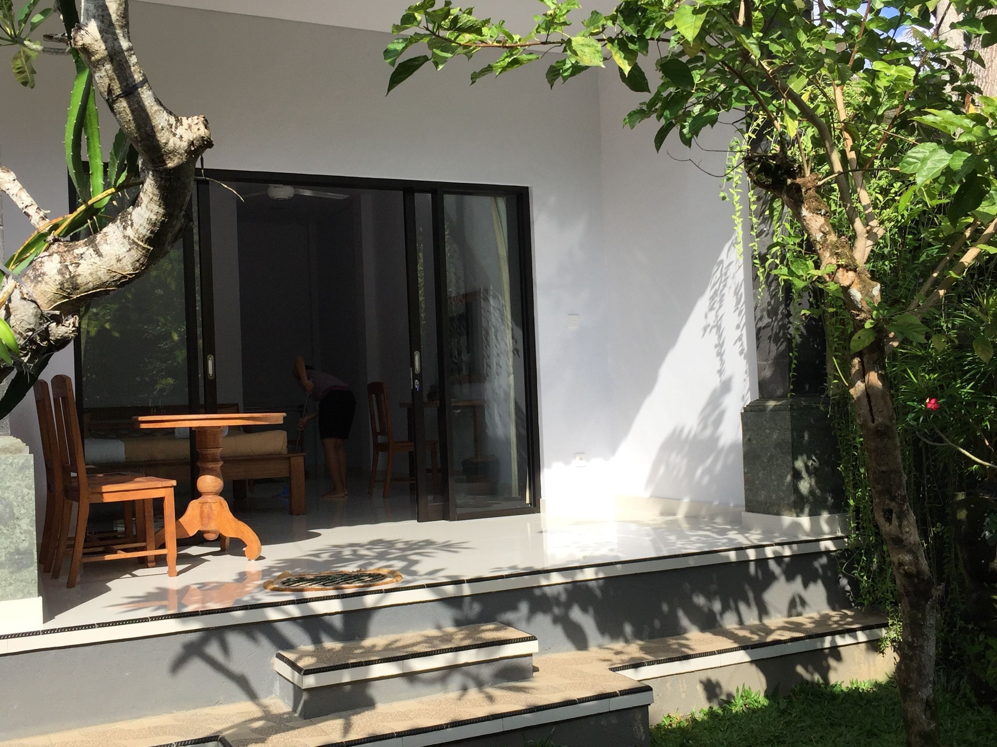 A modern outdoor seating area with a table and chairs, a glass door entrance, and a staircase leading to a covered area.