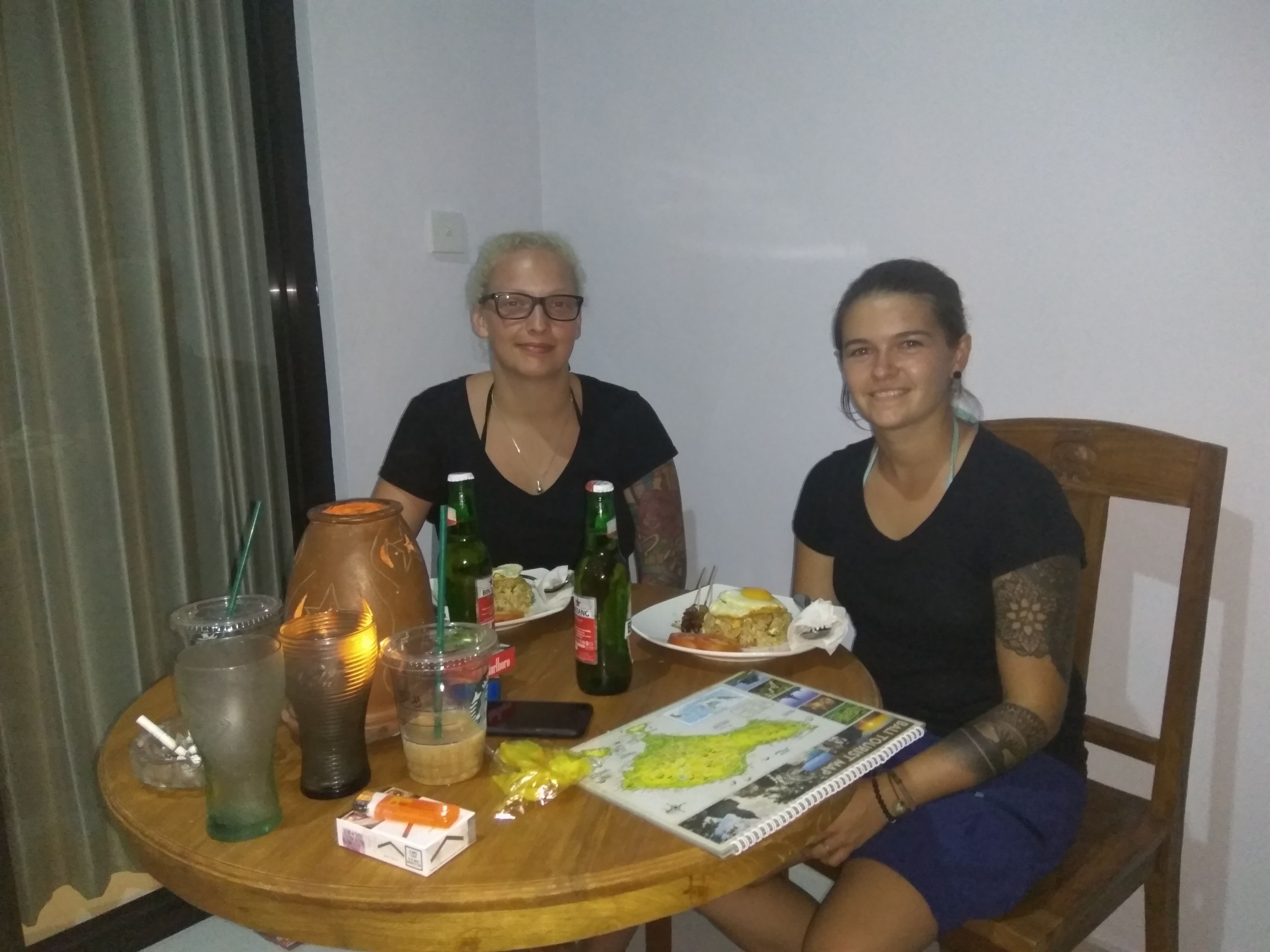 Two people seated at a wooden table with a map, bottles, and food.