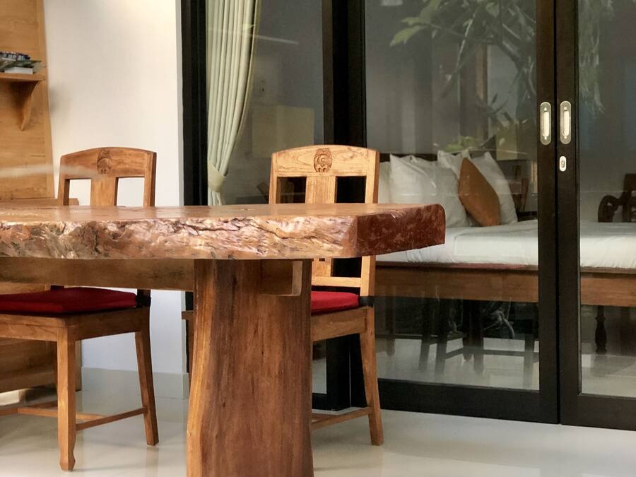 A dining area with a wooden table and chairs, a sliding glass door leading to a garden, and a wooden shelf with books.