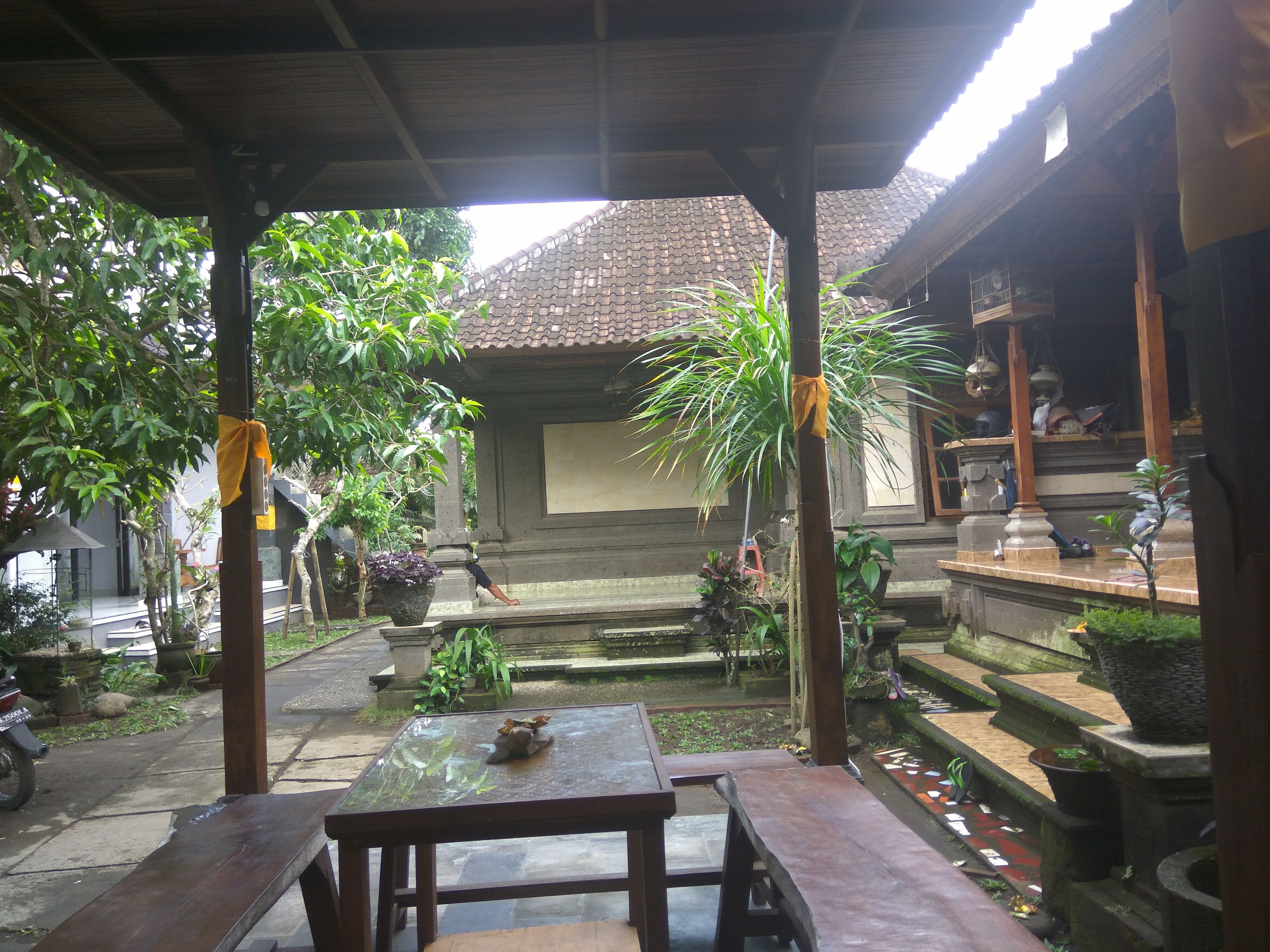 A covered outdoor area with a table and benches, surrounded by potted plants and a small water feature.