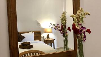 A mirror with a wooden frame reflecting a bed, pillows, a nightstand, a lamp, and a vase with flowers.
