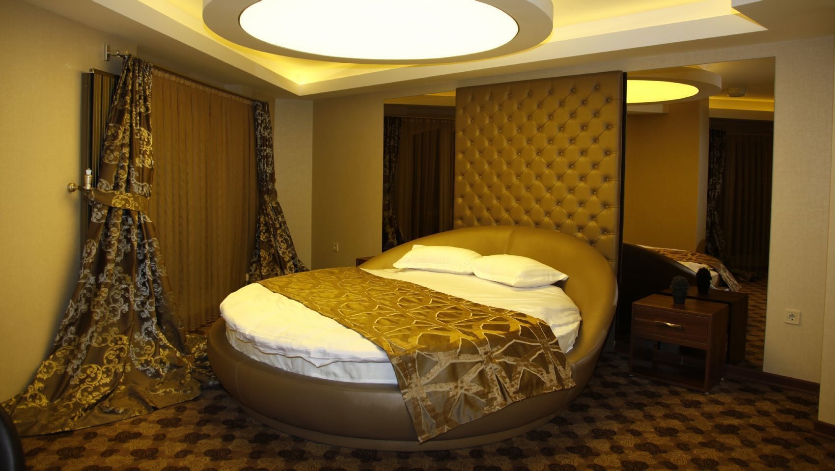 Una habitación de hotel espaciosa con una cama grande, cabecera capitonada y una lámpara de techo redonda.