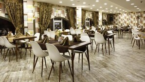 A spacious dining area with multiple tables and chairs, a patterned wall, and recessed ceiling lighting. - Feyzan Hotel (Corum)