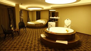 A hotel room with a large round bathtub, a bed, a chair, and a small table with a vase of flowers. - Feyzan Hotel (Corum)