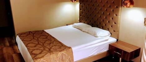 A neatly made bed with a patterned bedspread, a tufted headboard, and a bedside table with a lamp.