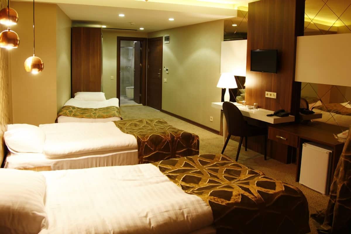 A hotel room with two beds, a desk, a chair, a television, and a bathroom visible through an open door.