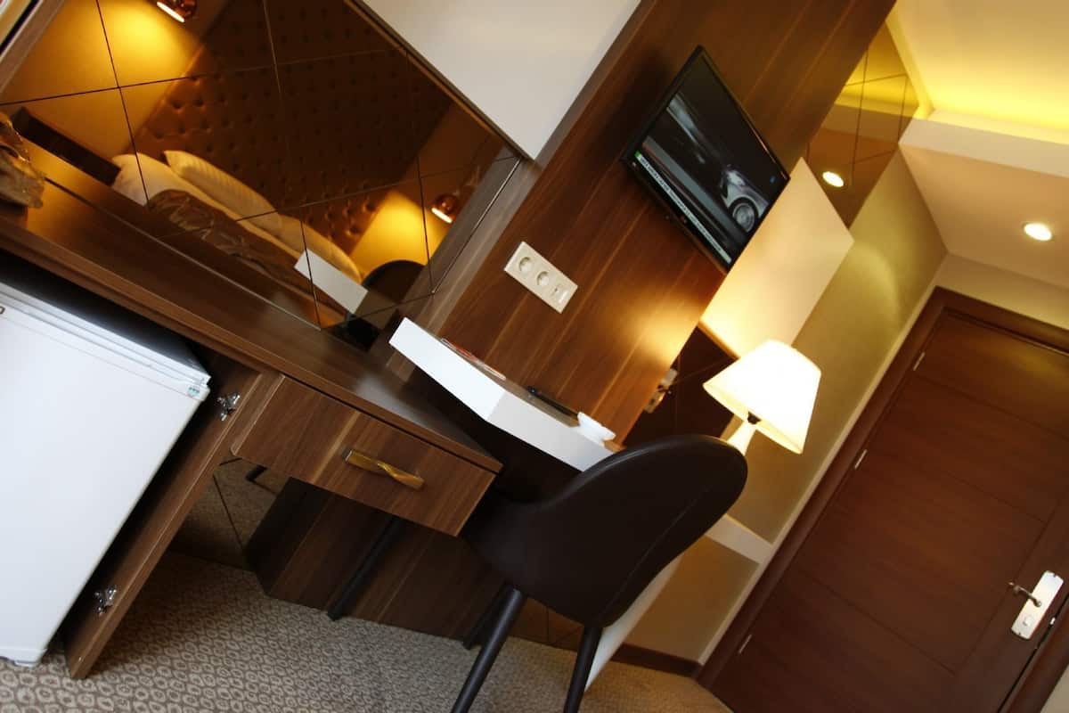 A hotel room with a wooden desk, a chair, a television mounted on the wall, and a door.