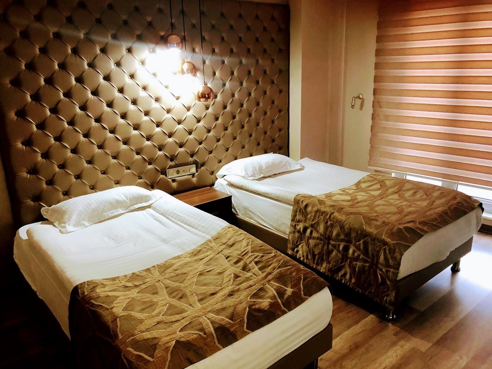 A hotel room with two beds, a tufted headboard, and a window with blinds.