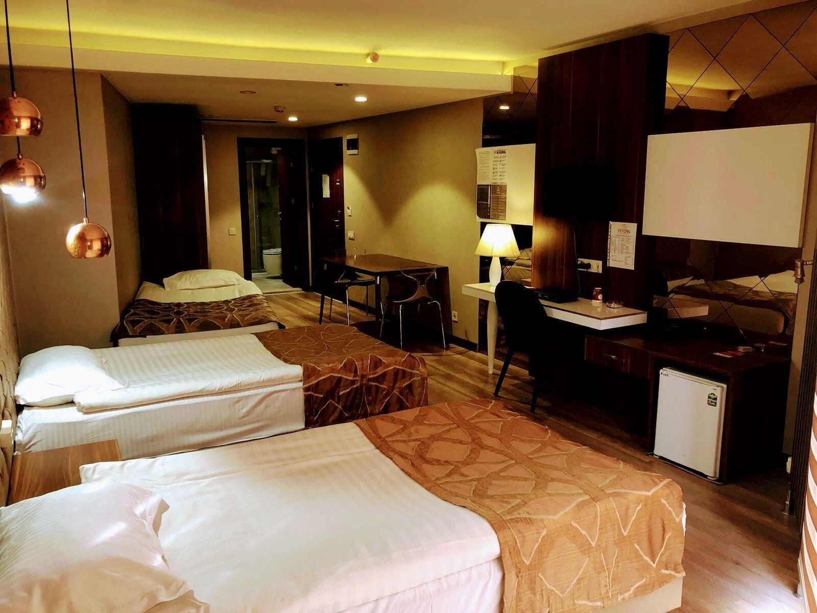 A hotel room with two single beds, a desk with a chair, a small refrigerator, and a television.