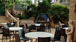 An outdoor patio with round tables and chairs, surrounded by potted plants and statues. - B&B Nicole (Palma di Montechiaro)