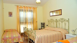 A bedroom with two beds, a window with curtains, a chair, and a bedside table. - B&B Nicole (Palma di Montechiaro)
