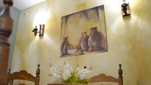 A dining area with a wooden table, chairs, a bowl of flowers, and a painting on the wall. - Hostal Toribio (Galaroza)
