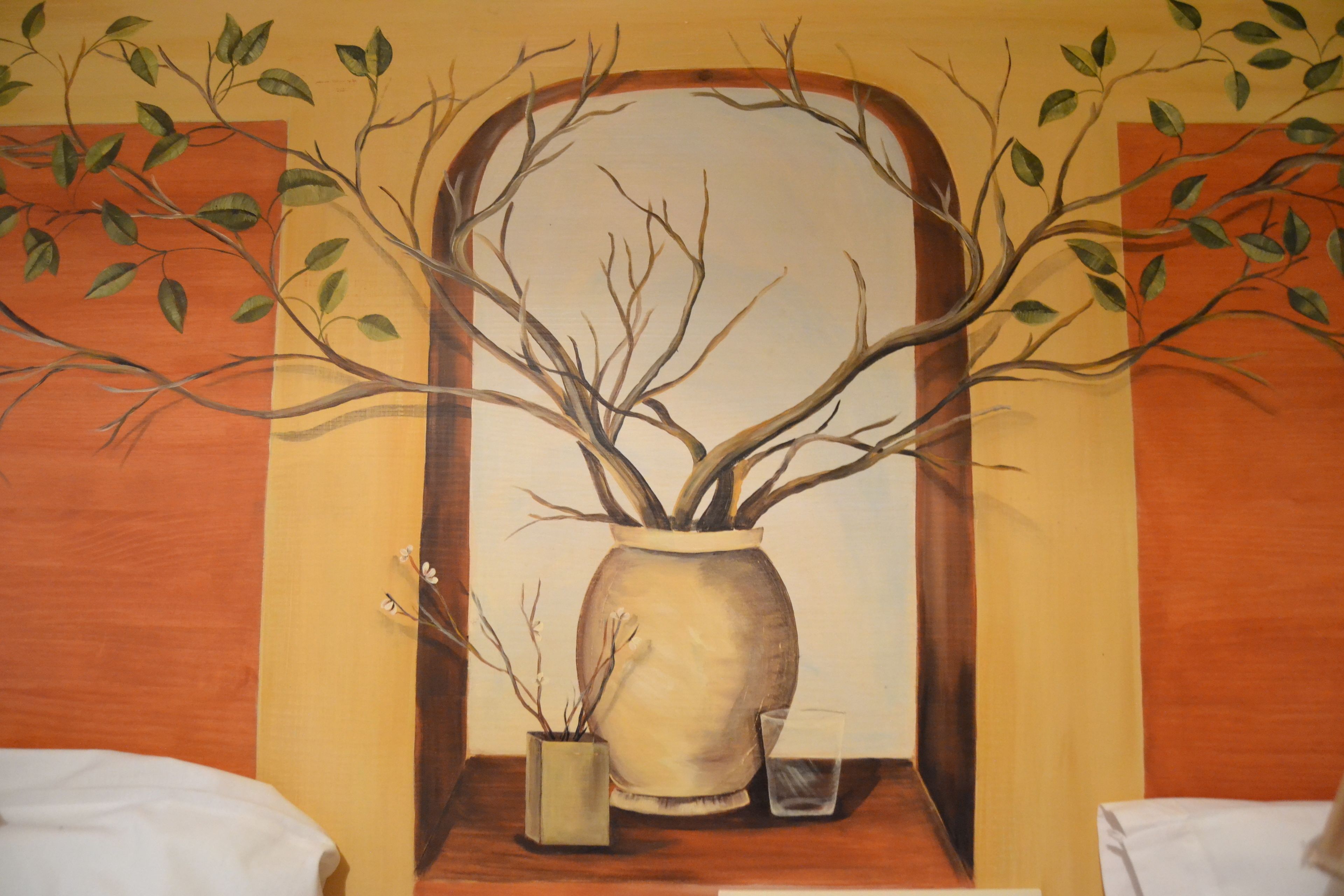A room with a large mirror reflecting a vase with branches and leaves.