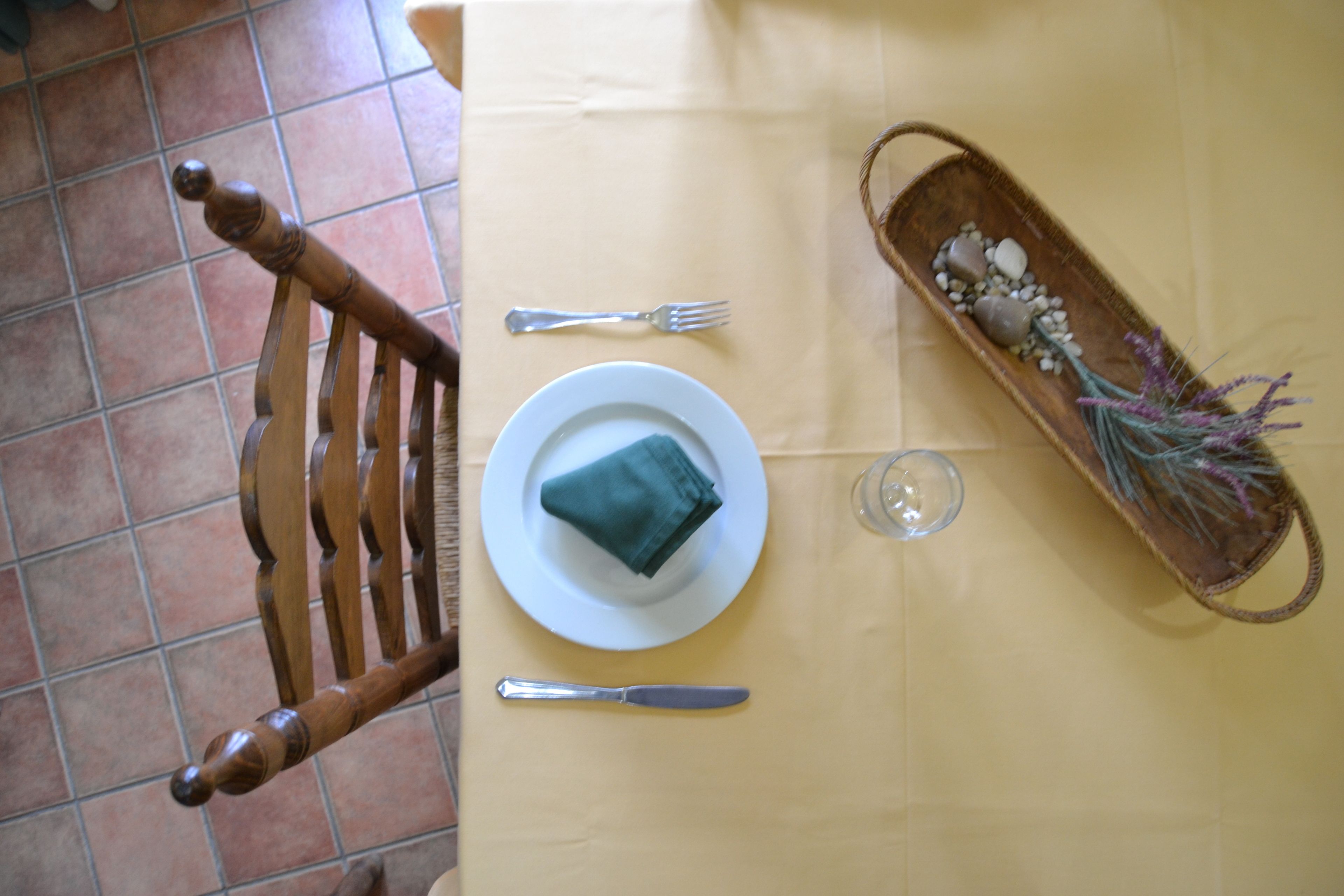 Una mesa de comedor con un plato, una servilleta doblada, un tenedor, un cuchillo y una bandeja decorativa con piedras y flores secas.
