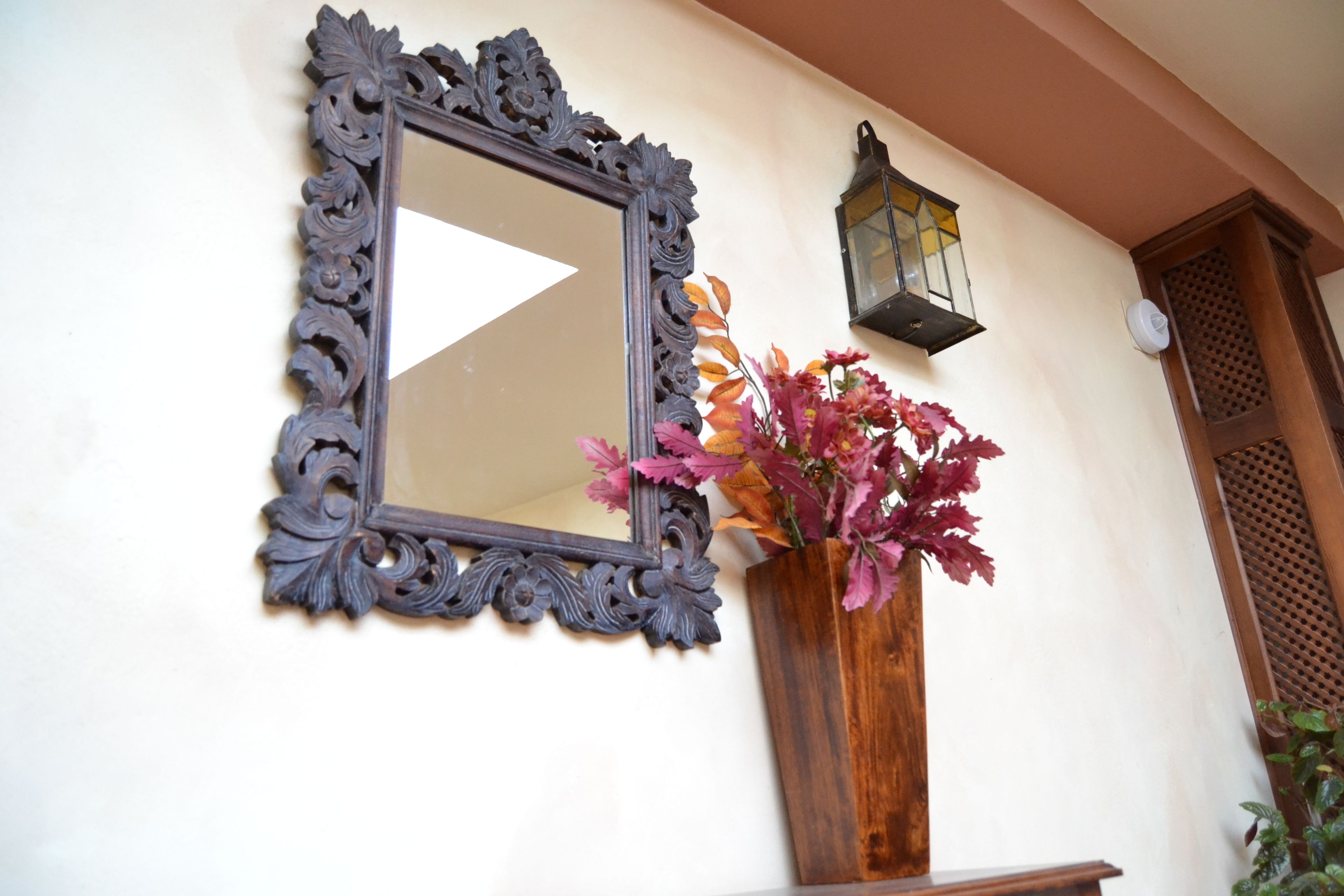 Un miroir avec un cadre orné, un vase en bois rempli de fleurs et une lanterne fixée au mur.