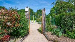 Un sendero en un jardín conduce a una zona de estar con una valla de madera y follaje a ambos lados.