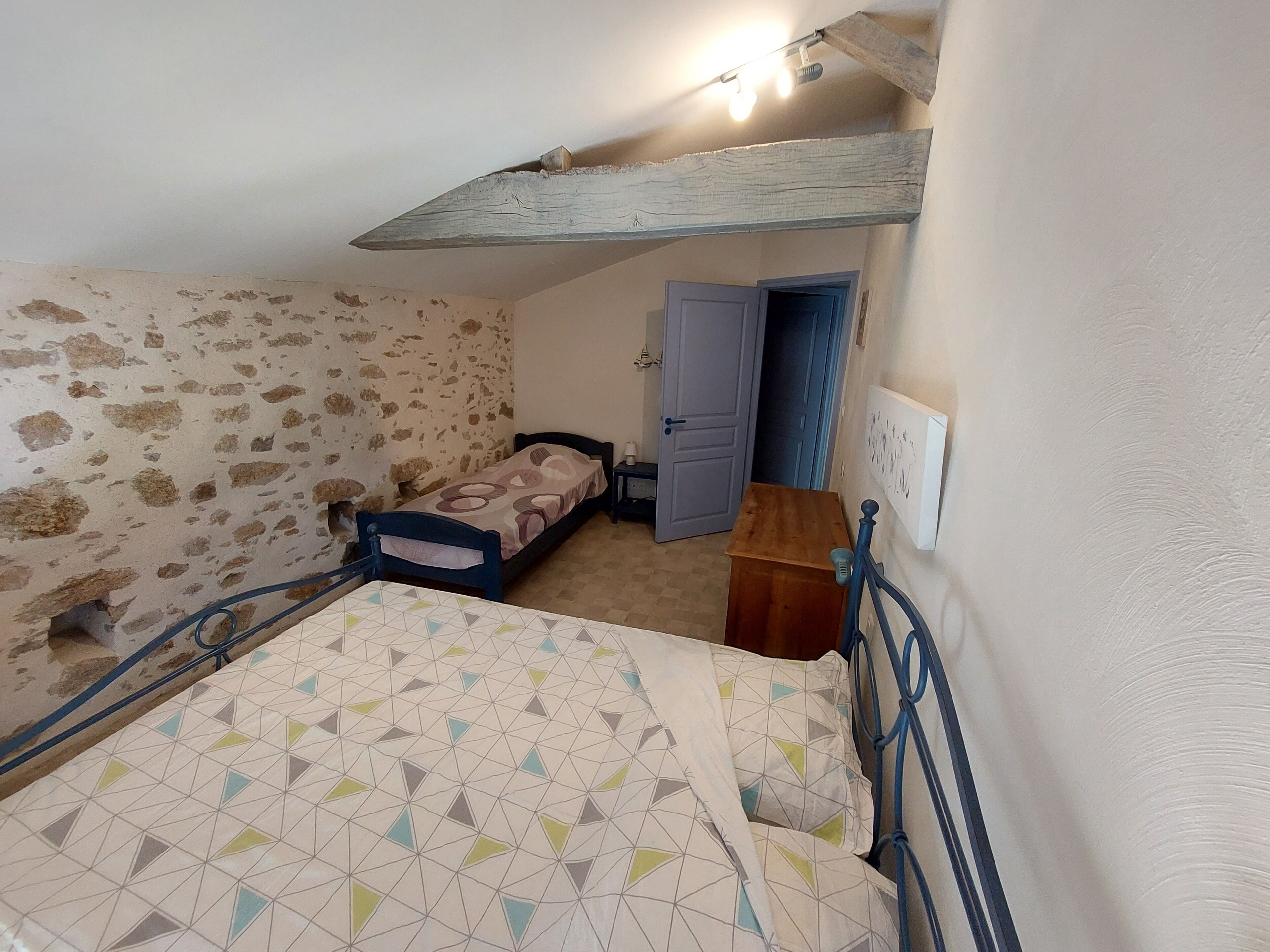 A bedroom with a bed, a wooden nightstand, a dresser, and a door leading to another room.