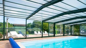 Una piscina interior con paredes de vidrio transparente, rodeada de sillas de descanso y vistas al exterior.