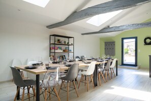 A dining area with a long table set for six, wooden chairs, a bookshelf, and a skylight.