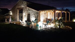 Edificio de piedra con un patio cubierto que tiene asientos al aire libre y una mesa.