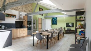 Una cocina moderna con armarios de madera, un comedor con una mesa larga y un televisor montado en la pared.