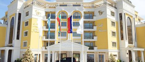 A multi-story hotel with a central entrance, balconies, and flags.