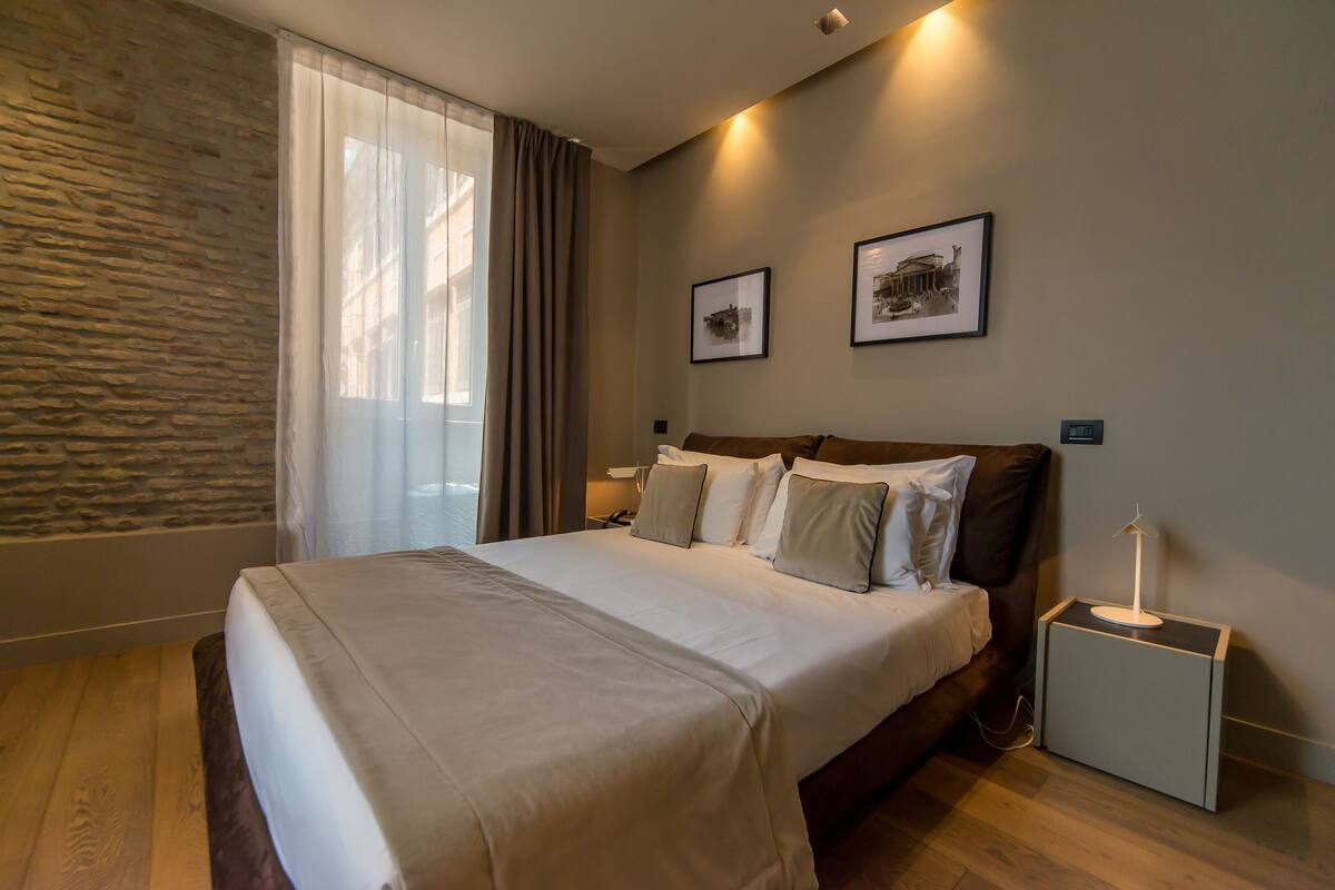 A neatly made bed with a headboard, a bedside table with a lamp, and two framed pictures on the wall.