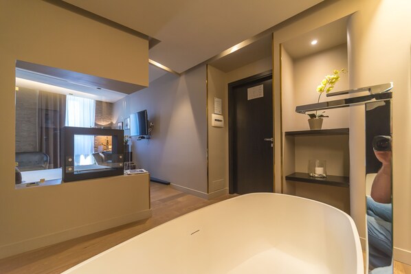 Un baño moderno con una bañera grande, un espejo, una repisa con una planta en maceta y una puerta con un letrero.