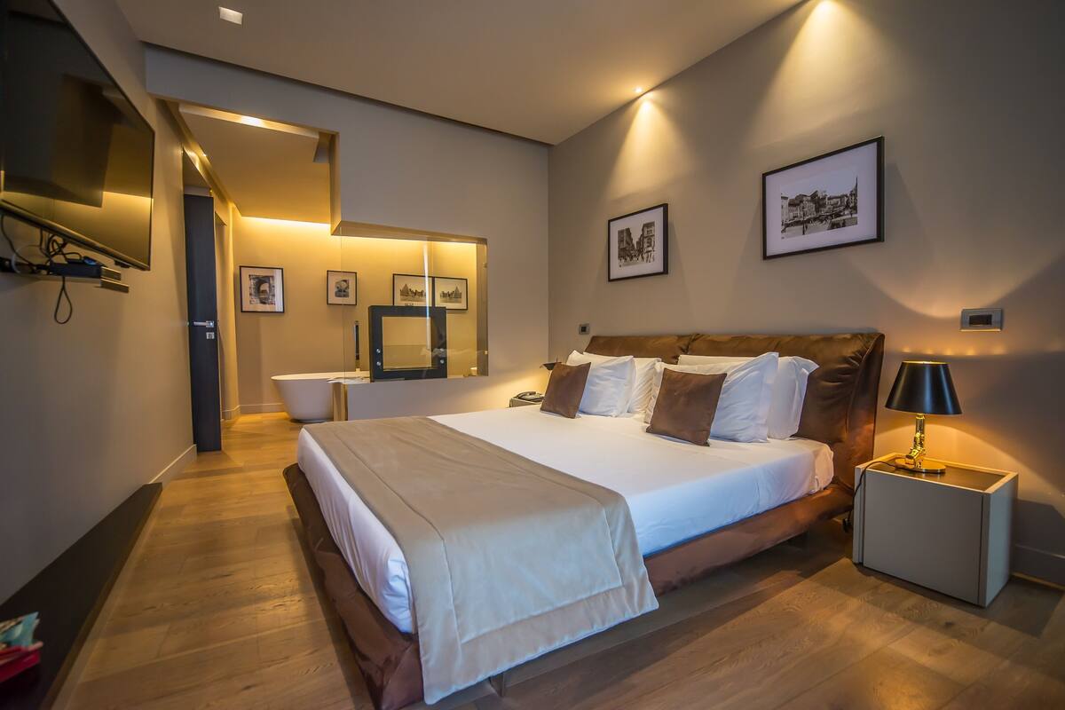 A modern hotel room with a large bed, bedside tables, a flat-screen TV, and framed pictures on the walls.