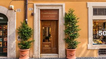 Entrada de un edificio con un cartel que dice 'Campomarzio Luxury Suites' y dos plantas en macetas a cada lado.