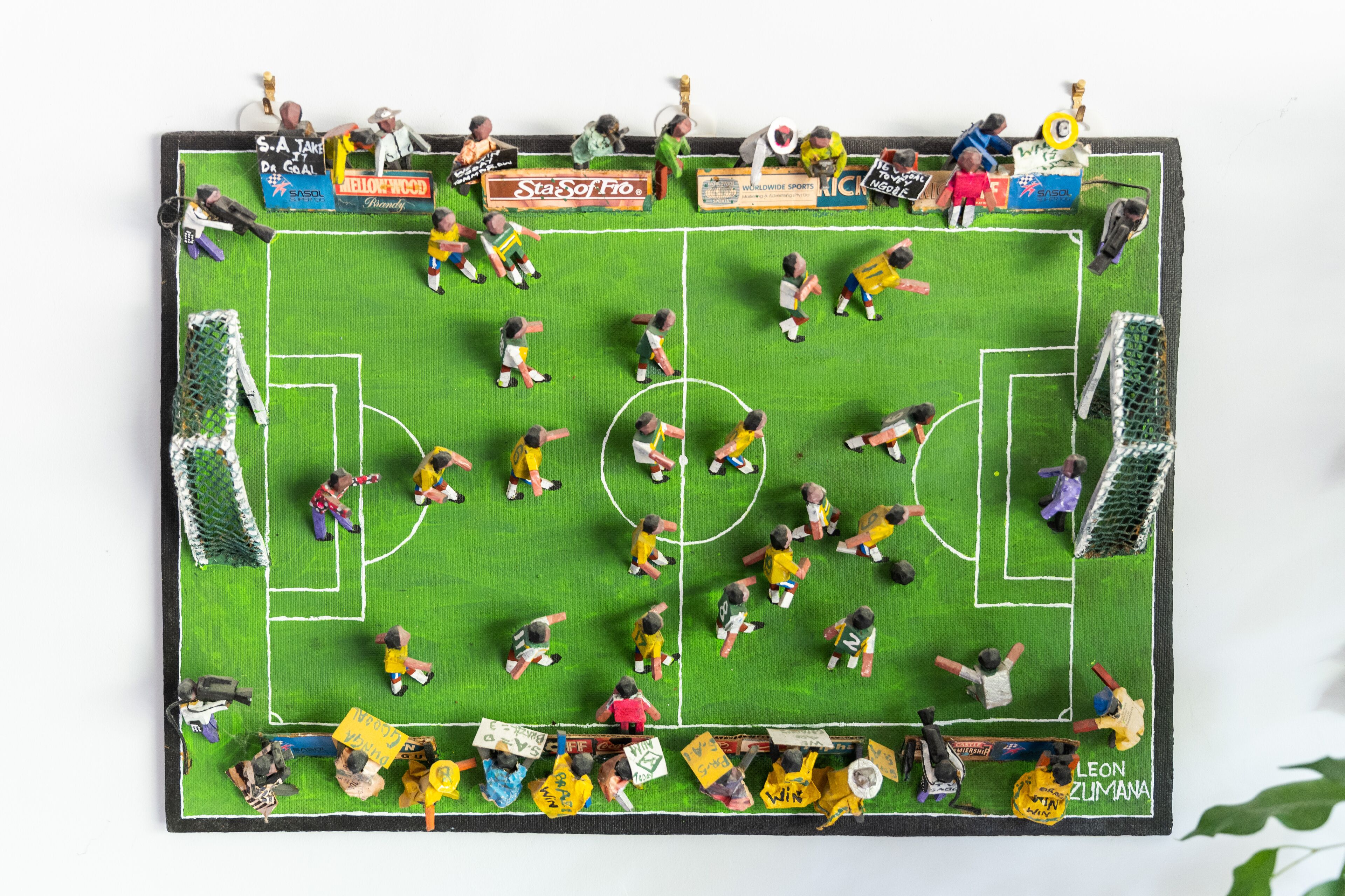 A miniature soccer field with players and goalkeepers in action, surrounded by various advertisements.