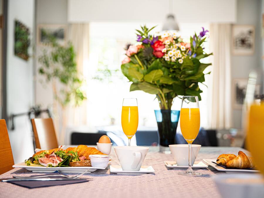 Une table dressée pour le petit-déjeuner, avec des croissants, un sandwich et du jus d’orange.