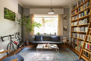 Un salón acogedor con una bicicleta, una estantería, un rincón de lectura junto a la ventana y una mesa de centro.