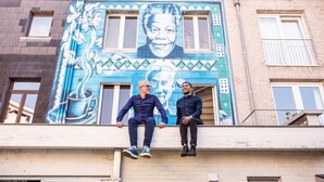 Two men sitting on a balcony with a mural of a woman and a coffee cup.
