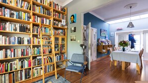 A spacious room with a large bookshelf filled with books, a comfortable armchair, a dining table with chairs, and a blue wall.