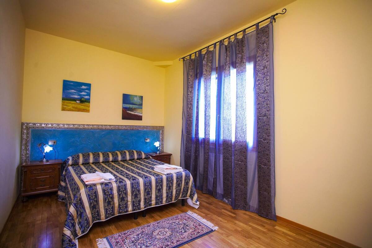 Een slaapkamer met een bed, twee nachtkastjes, een vloerkleed en een raam met gordijnen.
