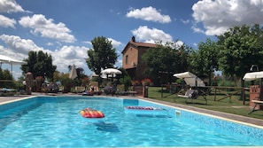 Une piscine entourée d’un bâtiment en briques et de verdure, avec des chaises longues et des parasols à proximité.