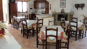 Un comedor con sillas y mesas de madera, una cocina al fondo y una chimenea.