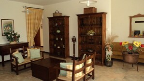 Una sala de estar con una mesa de centro de madera, dos sillas de madera, una estantería y una planta en maceta.