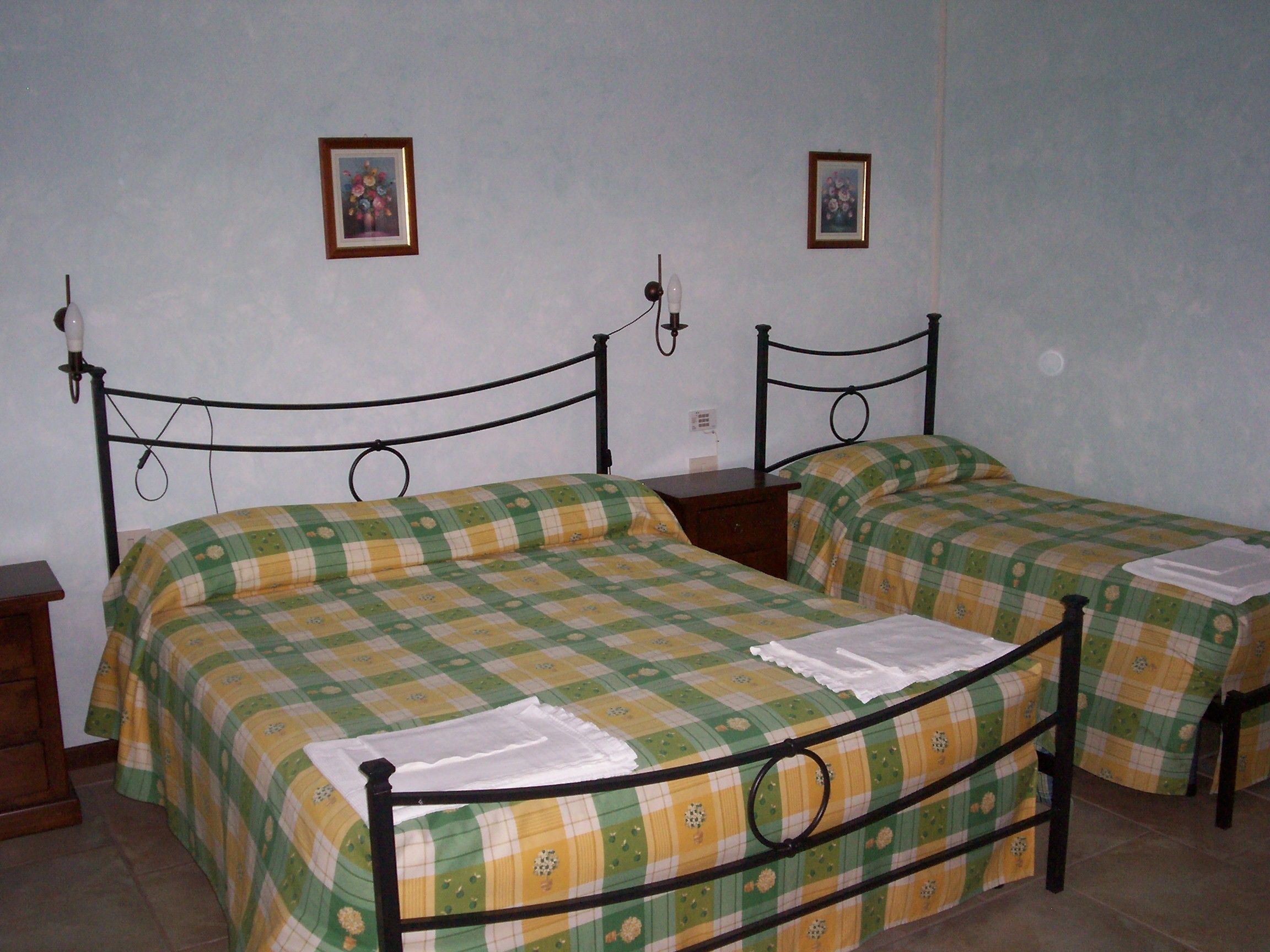 Una habitación con dos camas individuales, cada una con una colcha a cuadros y una almohada. Hay dos cuadros enmarcados en la pared sobre las camas.
