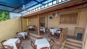 An outdoor patio with tables and chairs, covered by a blue roof, and a staircase leading to an upper level. - Pousada F7 (Campinas)