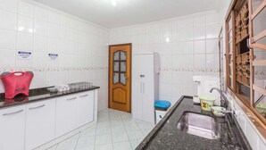A kitchen with white tiled walls, a wooden door, a sink, and a countertop with a red appliance. - Pousada F7 (Campinas)