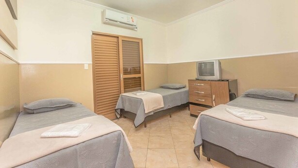 A small, clean room with two single beds, a wooden wardrobe, a television, and an air conditioning unit. - Pousada F7 (Campinas)